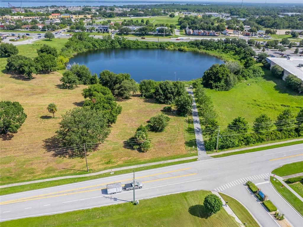 An aerial view shows a pond surrounded by green space, trees, and a paved road — 0000 DORA AVENUE, TAVARES, FL