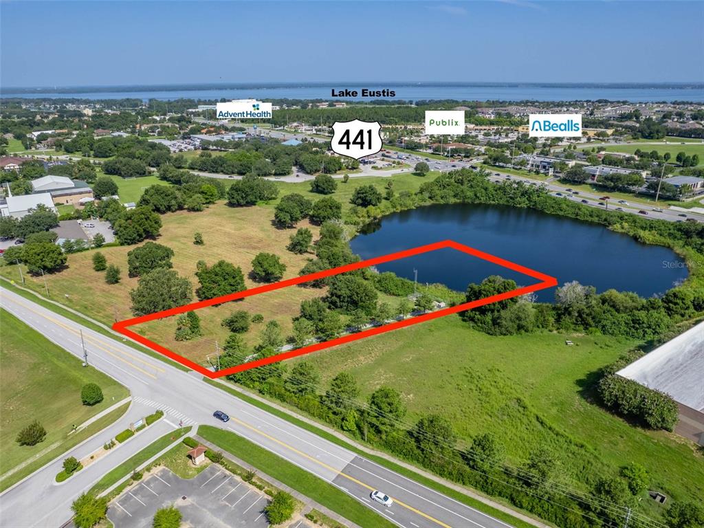 An aerial view shows a vacant, rectangular lot bordering a pond near a highway — 0000 DORA AVENUE, TAVARES, FL