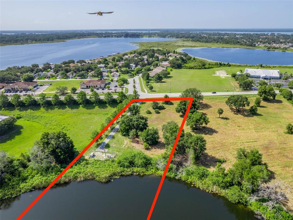 An aerial view shows a vacant, tree-lined lot bordering a lake with a road nearby — 0000 DORA AVENUE, TAVARES, FL