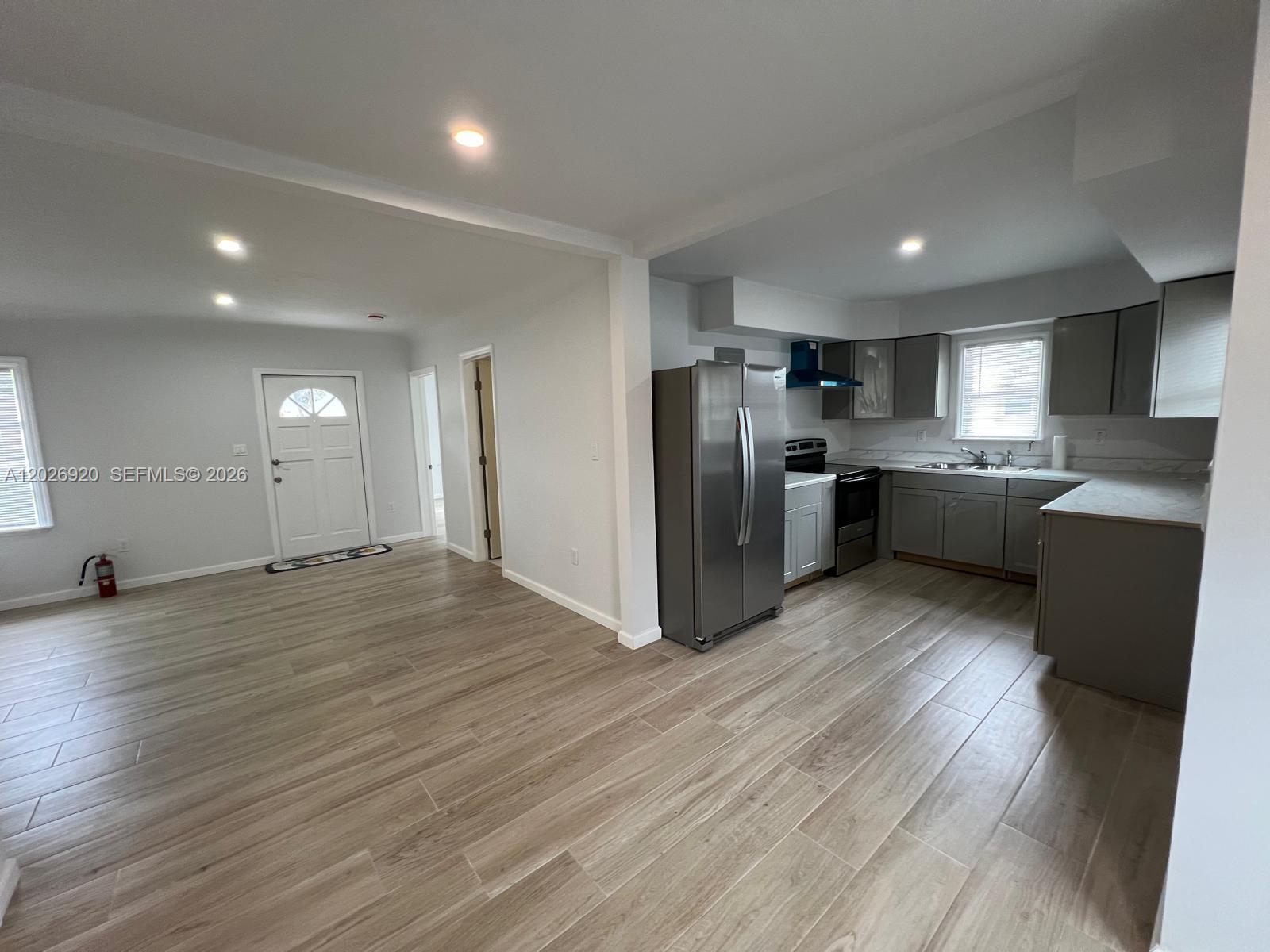A kitchen with gray cabinets and stainless steel appliances opens into a living area — MIAMI, FL