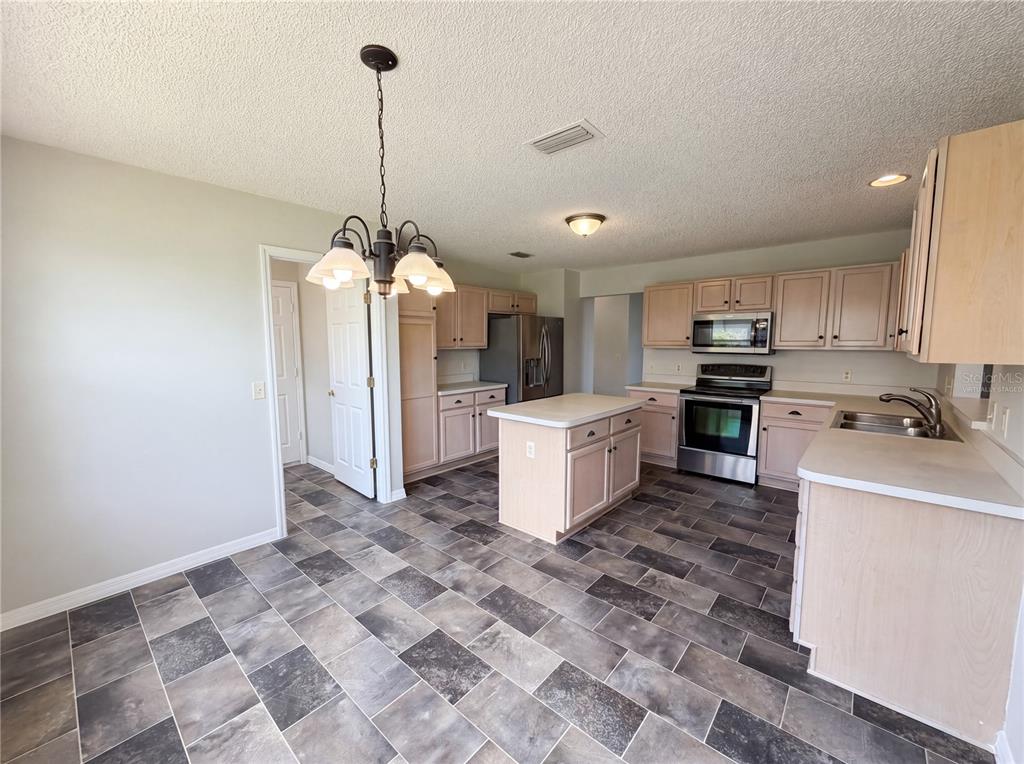 A kitchen with light wood cabinets, a central island, and gray tiled flooring — 1407 FIGUEROA STREET, THE VILLAGES, FL