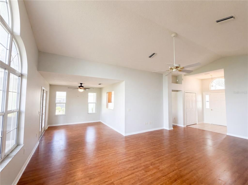 A spacious living area features light-colored walls, wood-look flooring, a ceiling fan, and large windows — 1407 FIGUEROA STREET, THE VILLAGES, FL