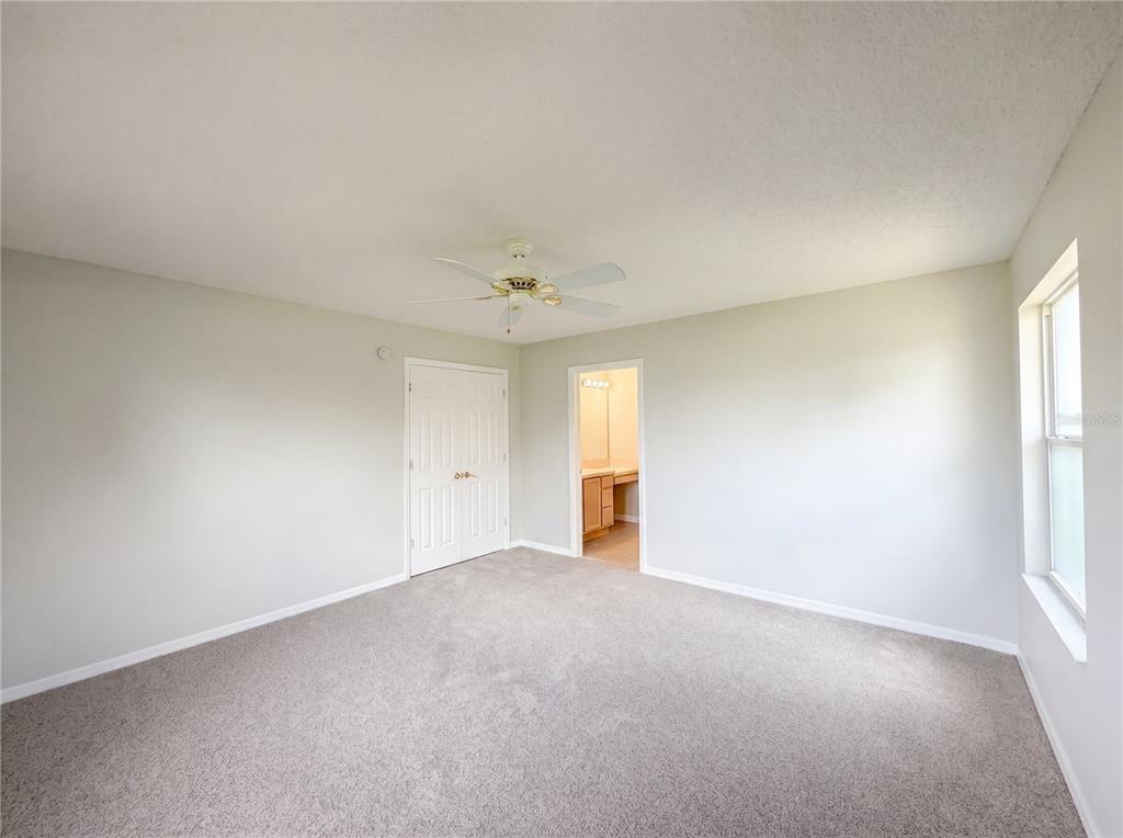 A bedroom with gray carpet, light walls, a ceiling fan, a closet, and an attached bathroom — 1407 FIGUEROA STREET, THE VILLAGES, FL