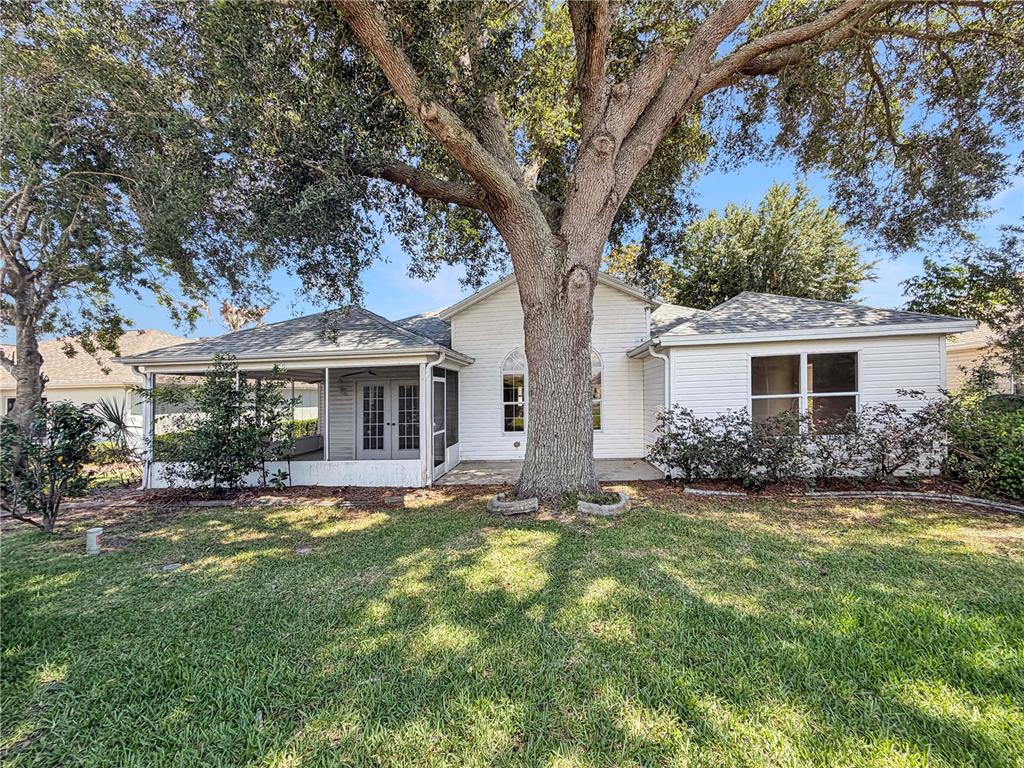 The rear exterior of a white house features a screened-in porch and a large oak tree — 1407 FIGUEROA STREET, THE VILLAGES, FL