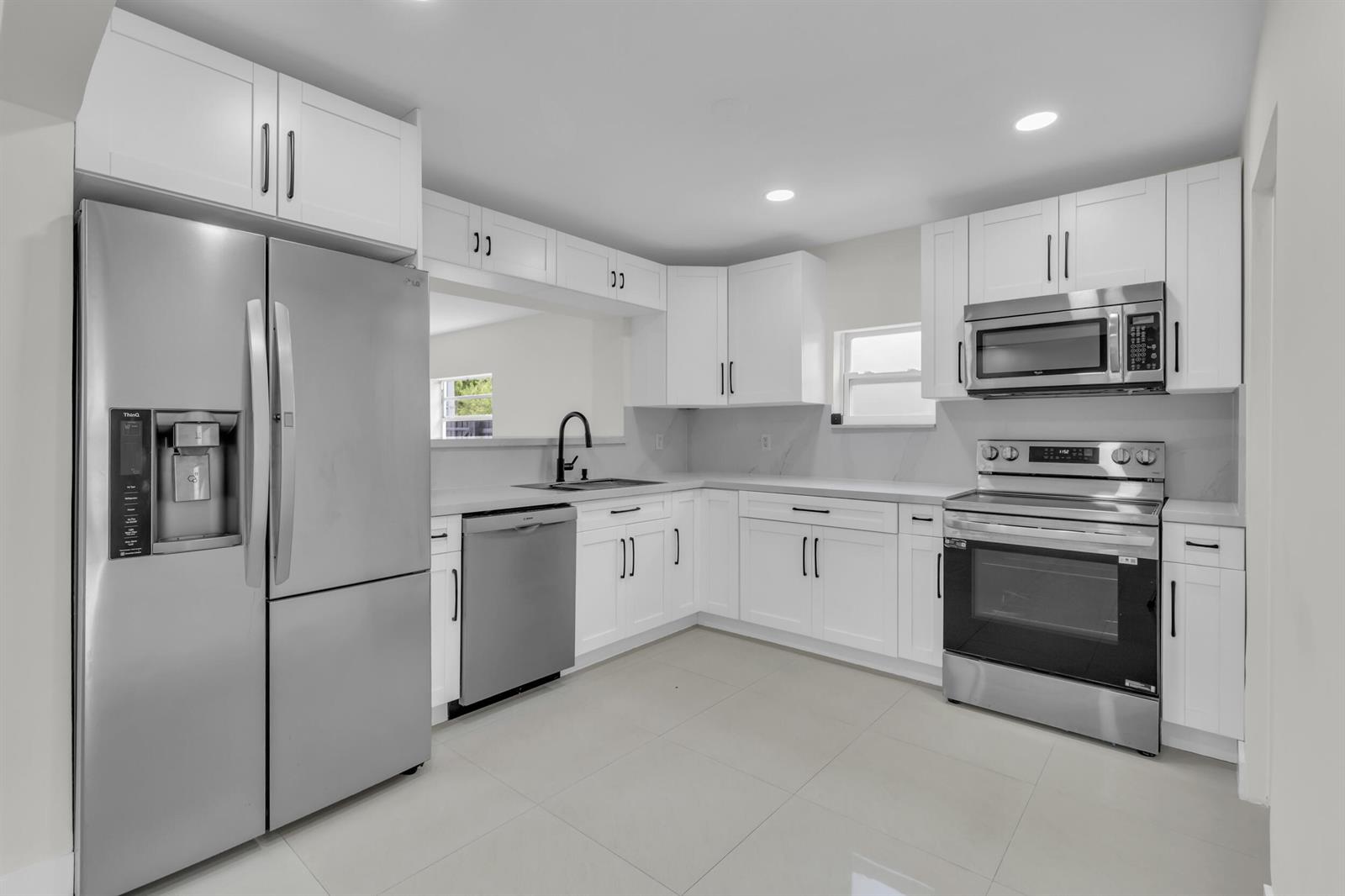 A modern kitchen features white shaker cabinets, stainless steel appliances, and light-colored tile flooring — 3262 Pierce Street, Hollywood FL 33021, HOLLYWOOD, FL