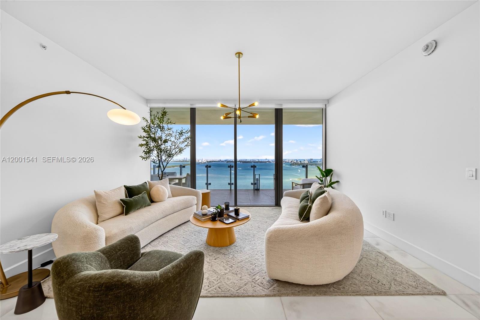 A modern living room features two curved sofas, a coffee table, and floor-to-ceiling ocean views — 700 NE 26 Ter # 3602, Miami FL 33137, MIAMI, FL
