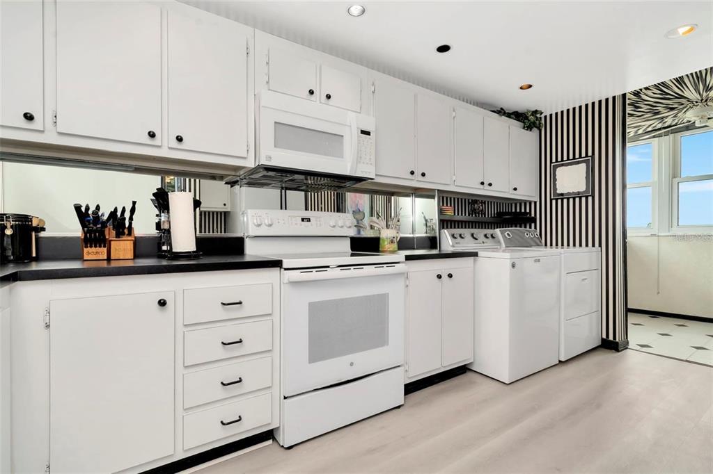 A kitchen features white cabinets, a white stove, a washer and dryer, and striped wallpaper — 15462 GULF BOULEVARD UNIT 508, MADEIRA BEACH, FL