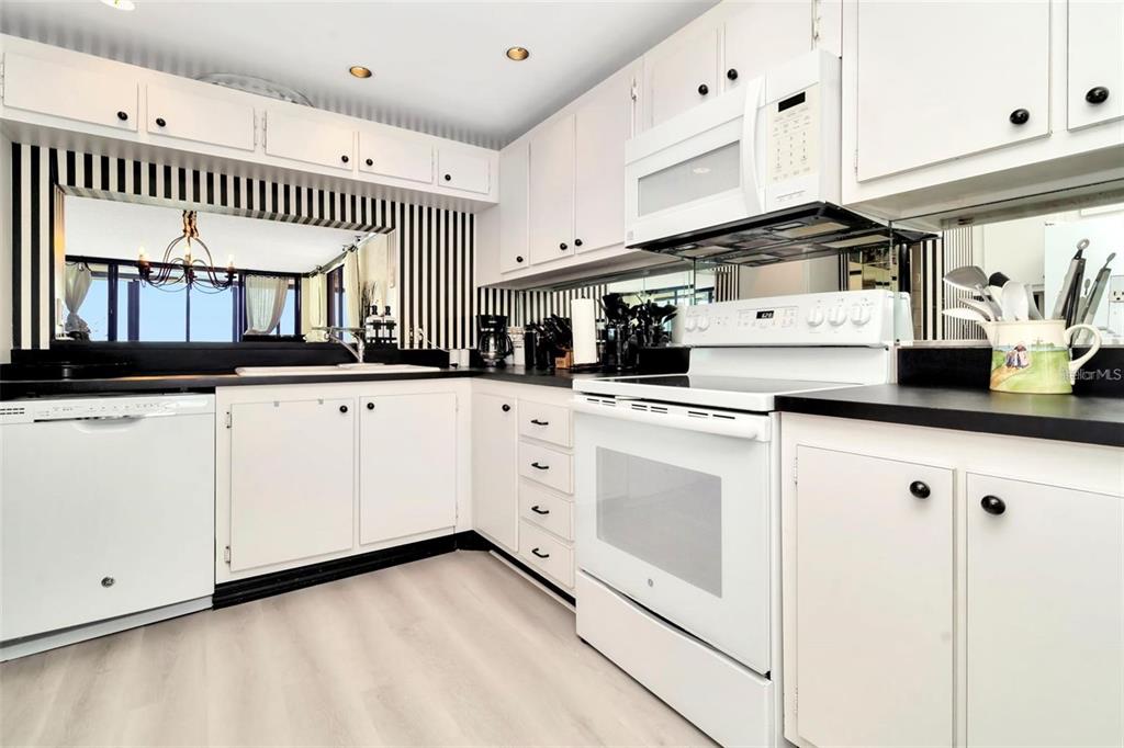 A kitchen features white cabinets, black countertops, and a black-and-white striped wall with a mirror — 15462 GULF BOULEVARD UNIT 508, MADEIRA BEACH, FL