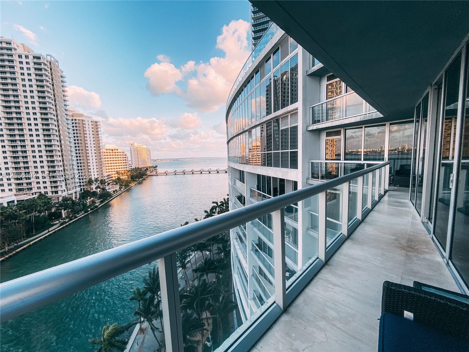 A high-rise balcony overlooks a waterway, a bridge, and surrounding residential buildings at sunset — 465 Brickell Ave # 1101, Miami FL 33131, MIAMI, FL