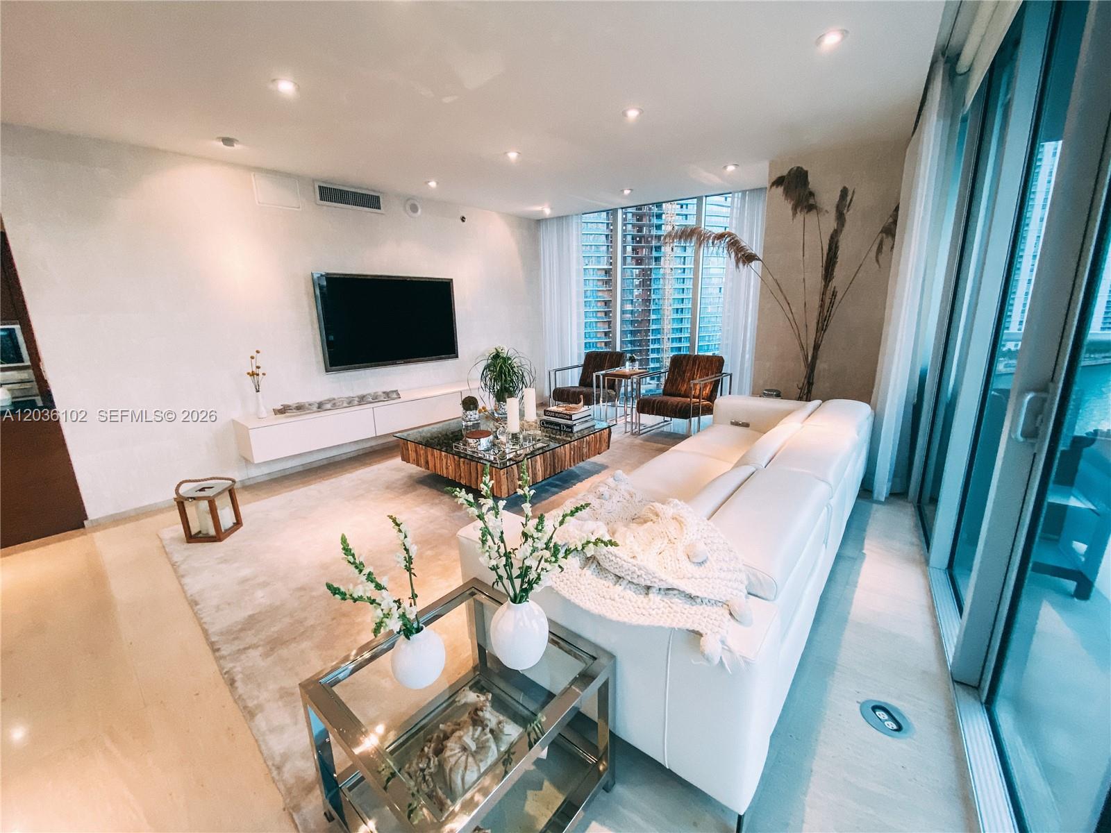 A modern living room features a white sofa, glass coffee table, and floor-to-ceiling windows — 465 Brickell Ave # 1101, Miami FL 33131, MIAMI, FL