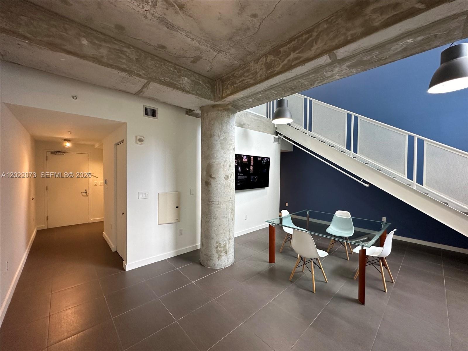 A dining area features a glass table, modern chairs, a concrete pillar, and a staircase — 3250 NE 1st Ave # 311, Miami FL 33137, MIAMI, FL