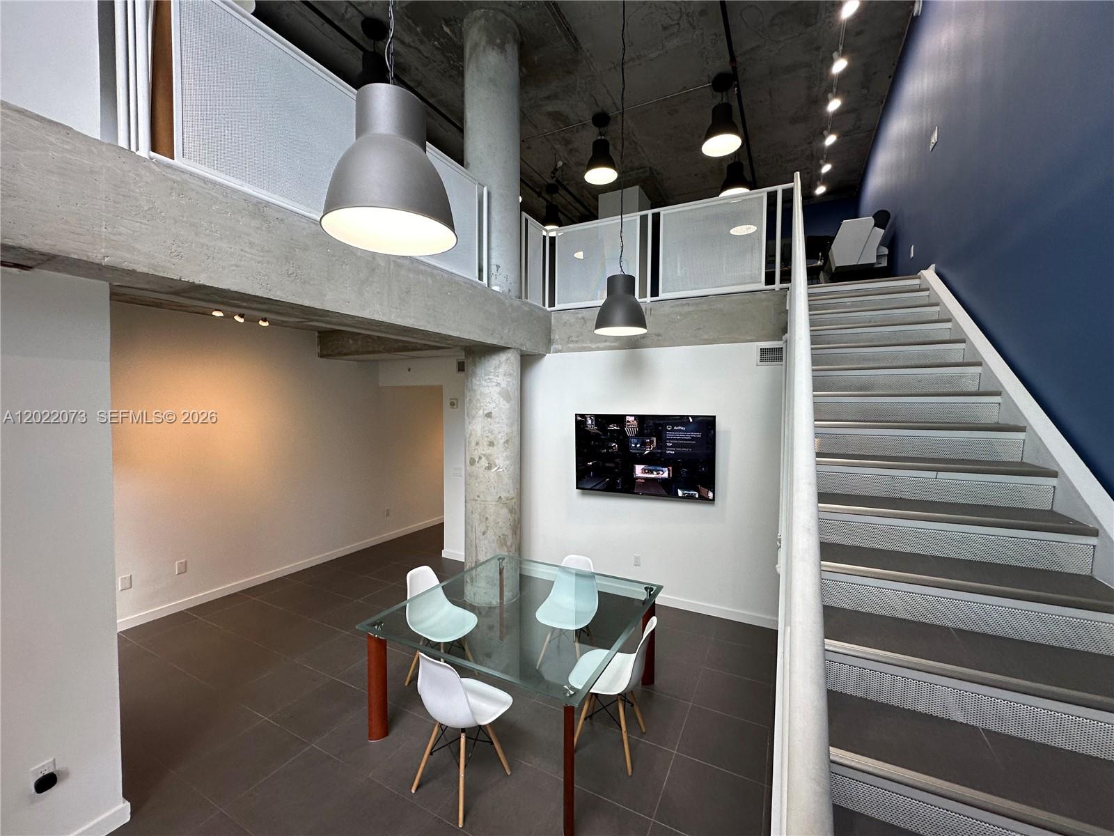 A dining area with a glass table and four chairs sits beneath a concrete loft — 3250 NE 1st Ave # 311, Miami FL 33137, MIAMI, FL
