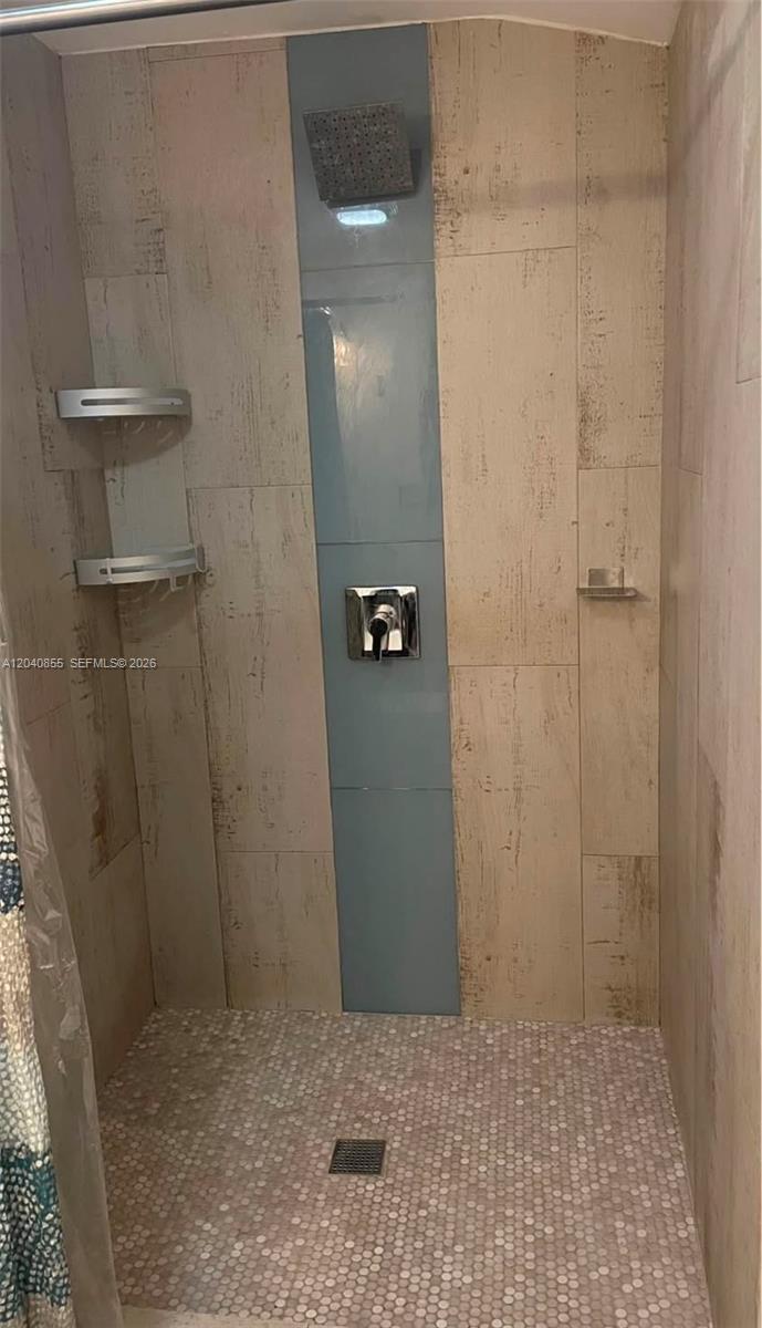 A shower stall features light wood-look tile walls, a blue accent panel, and pebble flooring — 420 NW 95th St # 420, Miami FL 33150, MIAMI, FL