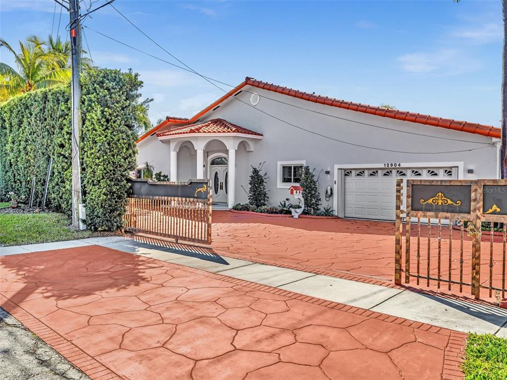 A single-story house with a terracotta tile roof and a gated, stamped concrete driveway — 12904 BANYAN ROAD, NORTH MIAMI, FL