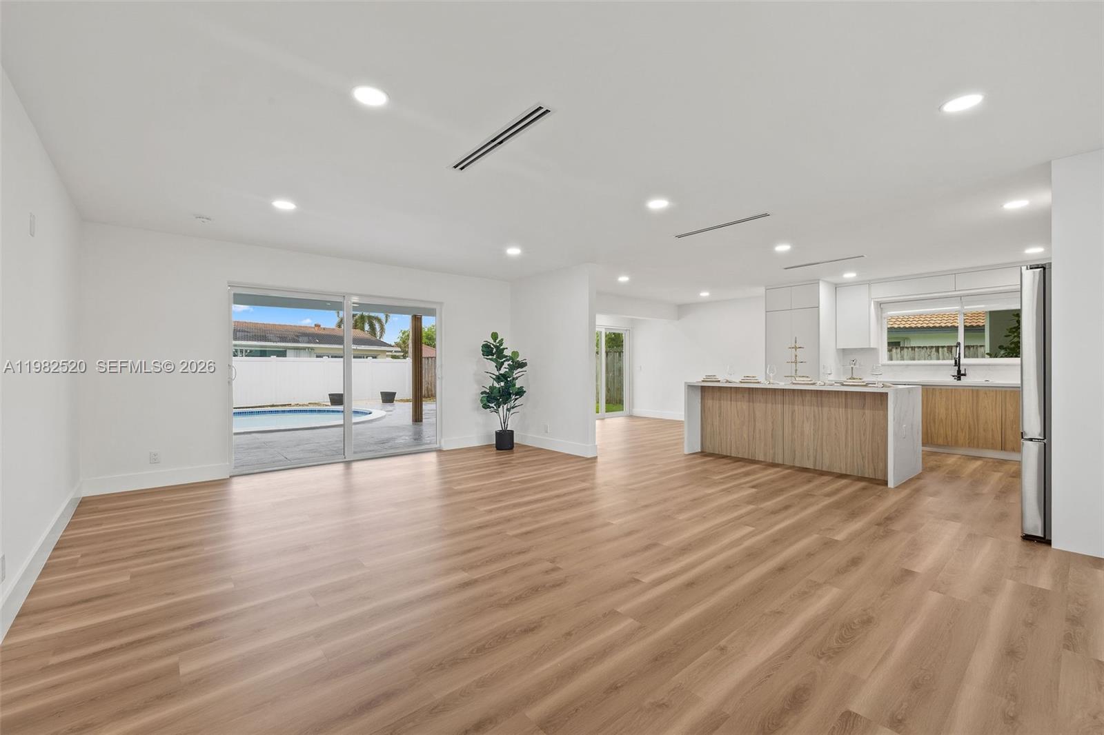 This open-concept living area features light wood flooring, a kitchen island, and sliding glass doors — 437 NW 13th Dr, Boca Raton FL 33486, BOCA RATON, FL