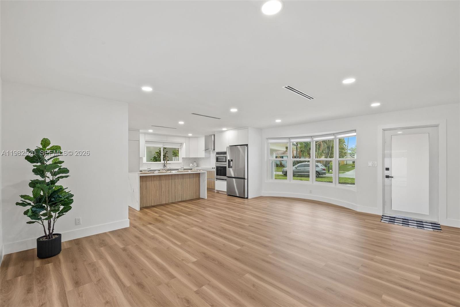 This open-concept kitchen and living area features light wood flooring, white cabinetry, and stainless appliances — 437 NW 13th Dr, Boca Raton FL 33486, BOCA RATON, FL