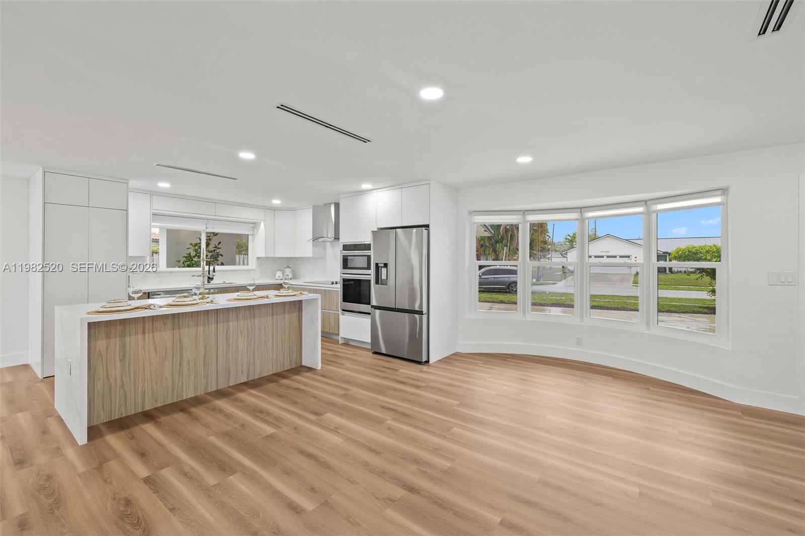 A modern kitchen features a wood-paneled island, white cabinetry, stainless steel appliances, and bay windows — 437 NW 13th Dr, Boca Raton FL 33486, BOCA RATON, FL