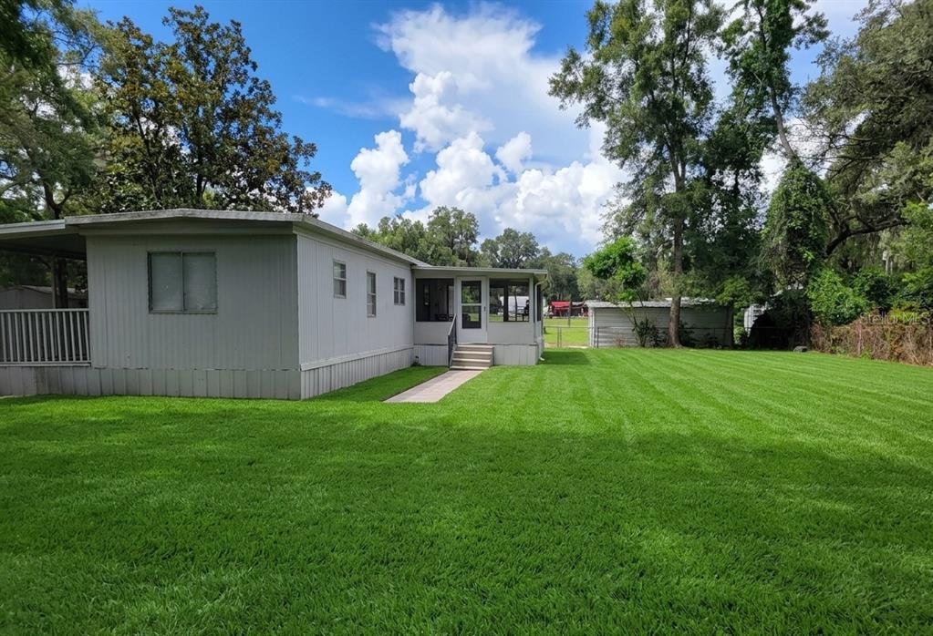 A light-colored mobile home with a screened-in porch sits on a large, mowed grassy lawn — 17855 SE 15TH COURT, SUMMERFIELD, FL