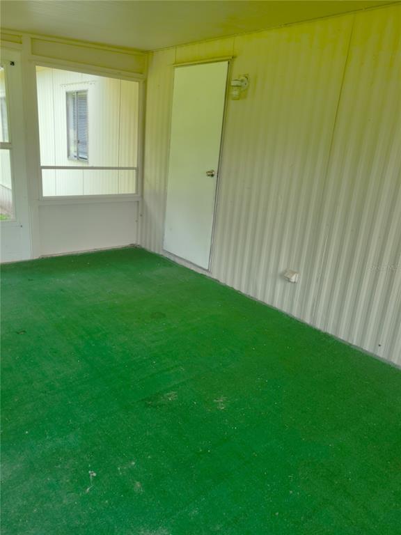 A covered porch with green outdoor carpeting, a white door, and a screened window — 17855 SE 15TH COURT, SUMMERFIELD, FL