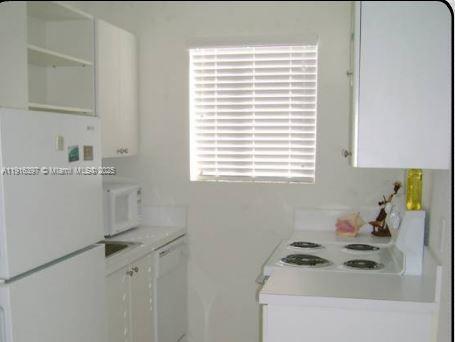 A small white kitchen features a refrigerator, electric stove, microwave, and white cabinetry — 3680 Oak Ave # 6, Miami FL 33133, MIAMI, FL
