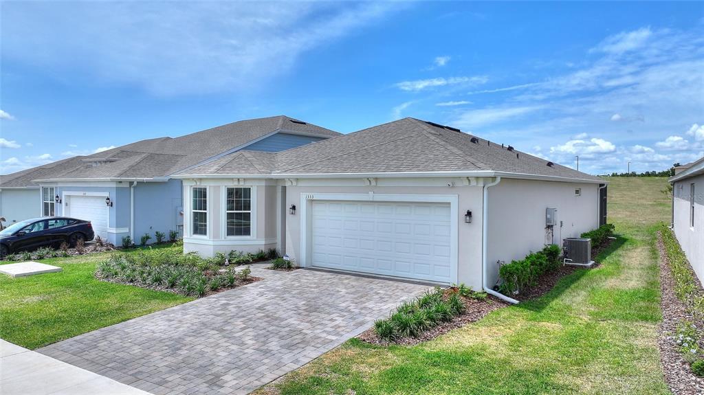 A single-story house with a white garage, beige stucco siding, and a paved driveway — 1333 ZESTY CITRUS LN, MINNEOLA, FL