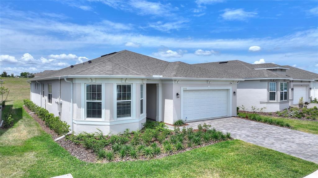 A single-story house with a beige stucco exterior, a gray shingled roof, and a garage — 1333 ZESTY CITRUS LN, MINNEOLA, FL