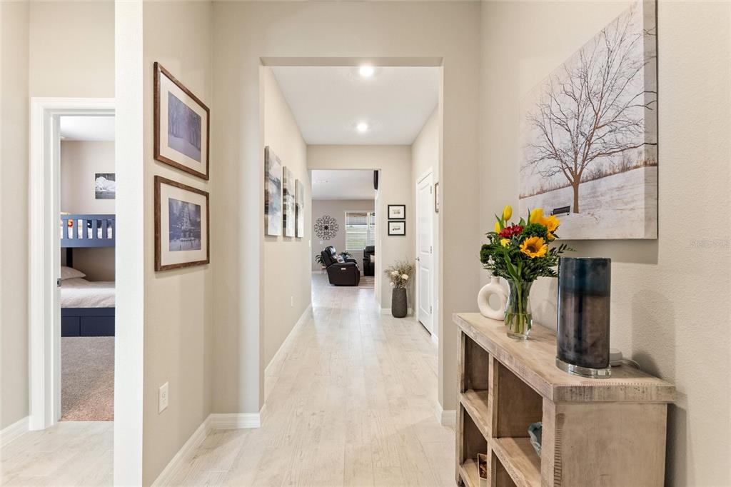 A hallway with light-colored tile flooring leads toward a living area with a console table — 1333 ZESTY CITRUS LN, MINNEOLA, FL