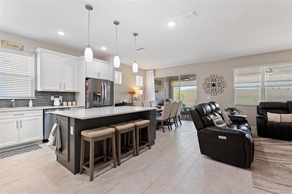 An open-concept kitchen and living area features a dark island, white cabinets, and tile flooring — 1333 ZESTY CITRUS LN, MINNEOLA, FL