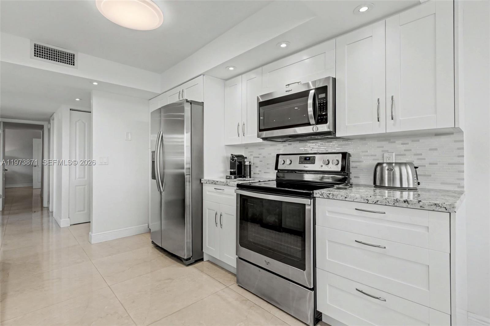 A modern kitchen features white cabinets, stainless steel appliances, and light-colored granite countertops — 2017 S Ocean Dr # 209, Hallandale Beach FL 33009, HALLANDALE BEACH, FL
