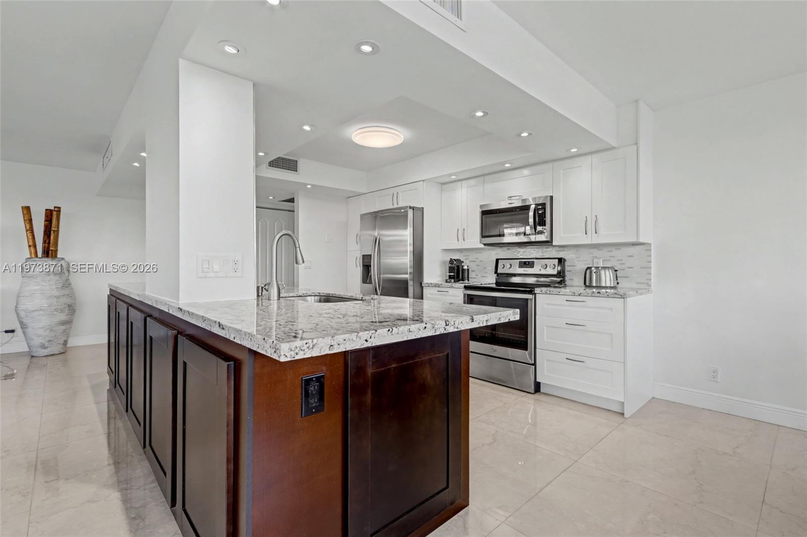 A kitchen features dark wood cabinetry, a granite island, white upper cabinets, and stainless appliances — 2017 S Ocean Dr # 209, Hallandale Beach FL 33009, HALLANDALE BEACH, FL