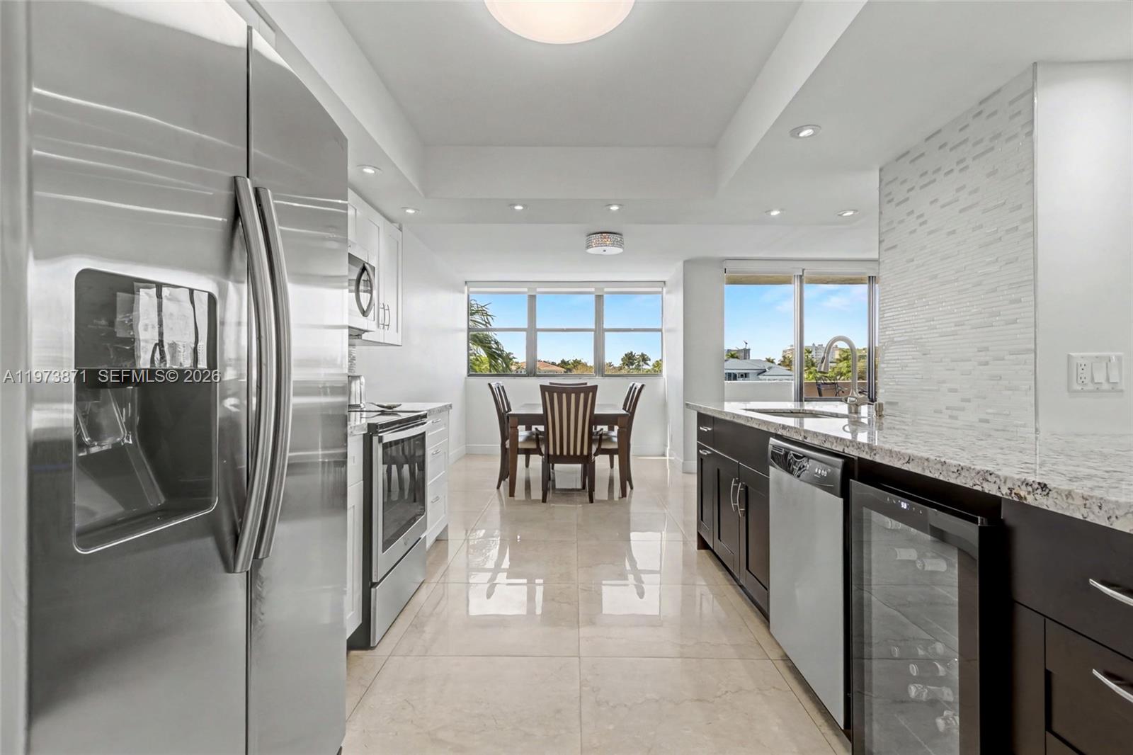 A modern kitchen with stainless steel appliances, dark cabinets, and a dining area with windows — 2017 S Ocean Dr # 209, Hallandale Beach FL 33009, HALLANDALE BEACH, FL