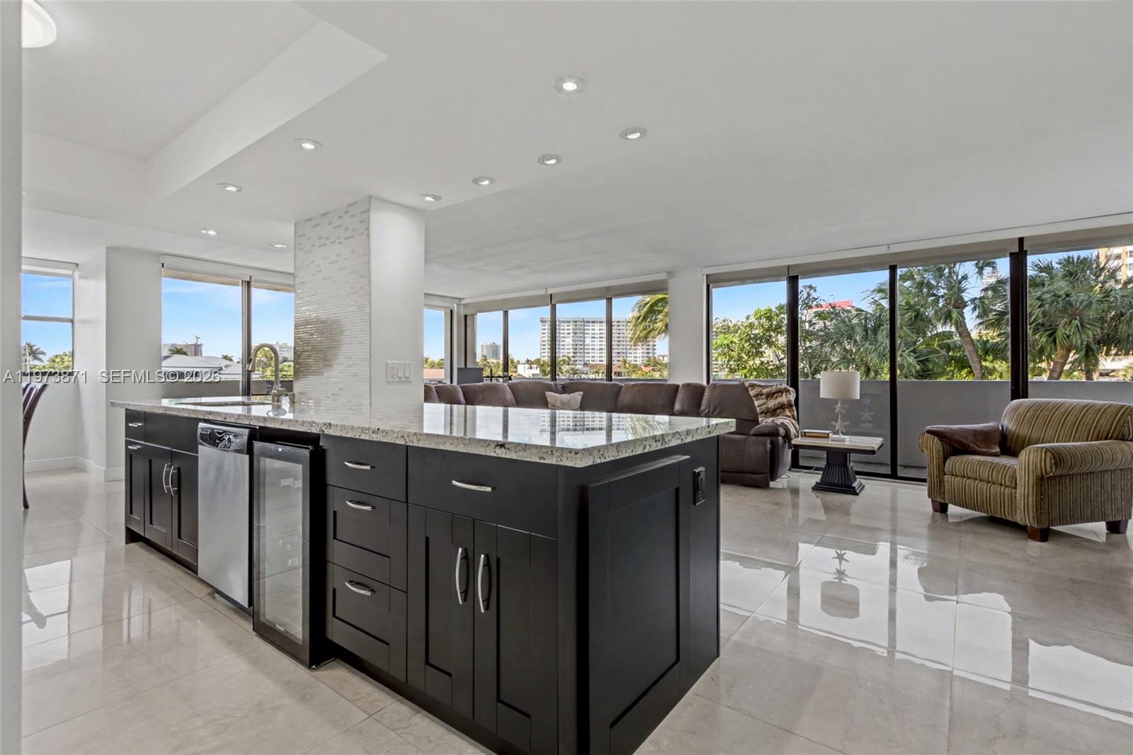 A modern kitchen island with dark cabinets and granite countertops sits in an open-concept living area — 2017 S Ocean Dr # 209, Hallandale Beach FL 33009, HALLANDALE BEACH, FL