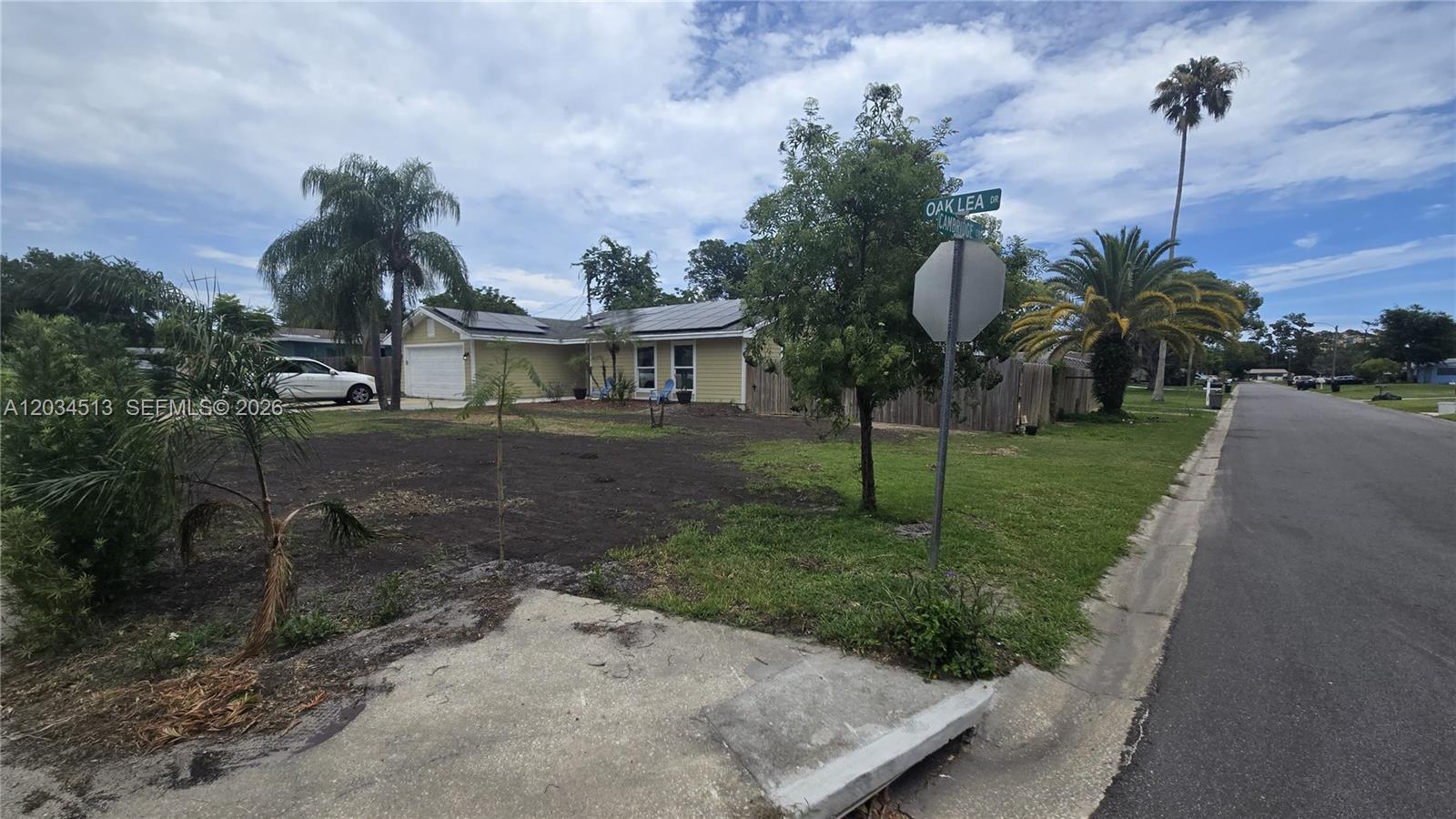 A yellow single-story house with solar panels sits on a corner lot with bare soil — 2845 OAK LEA DR, Daytona FL 32119, DAYTONA, FL