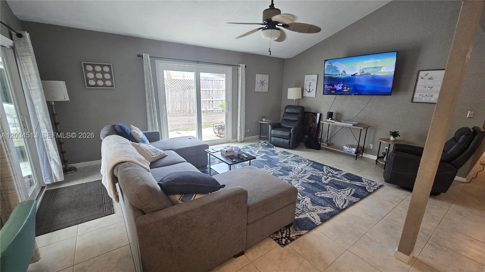 A living room features a gray sectional sofa, a blue starfish rug, and a wall-mounted television — 2845 OAK LEA DR, Daytona FL 32119, DAYTONA, FL