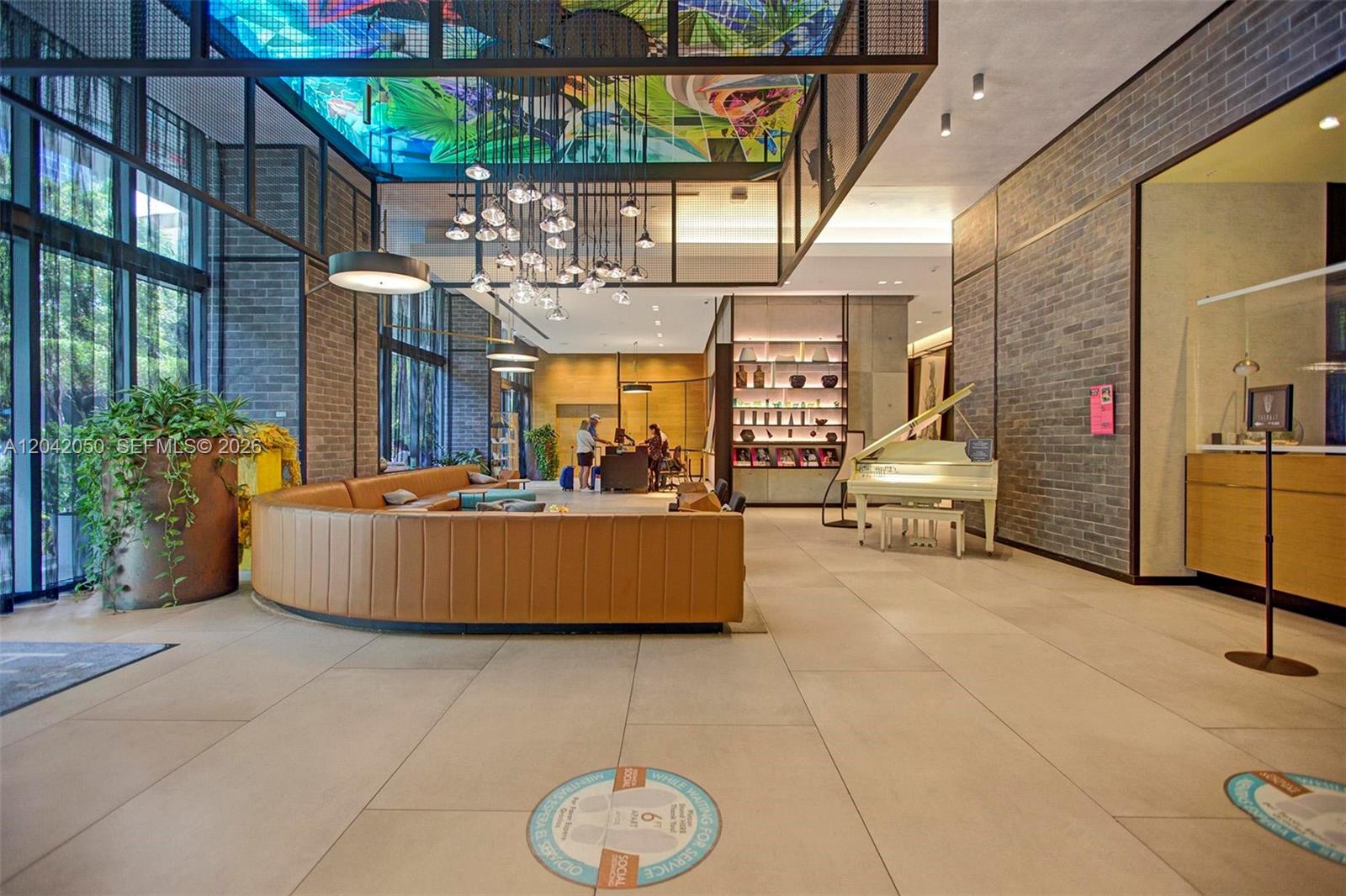 A modern lobby features a curved tan sofa, a white piano, and a colorful ceiling mural — 121 NE 34th St # 2205, Miami FL 33137, MIAMI, FL