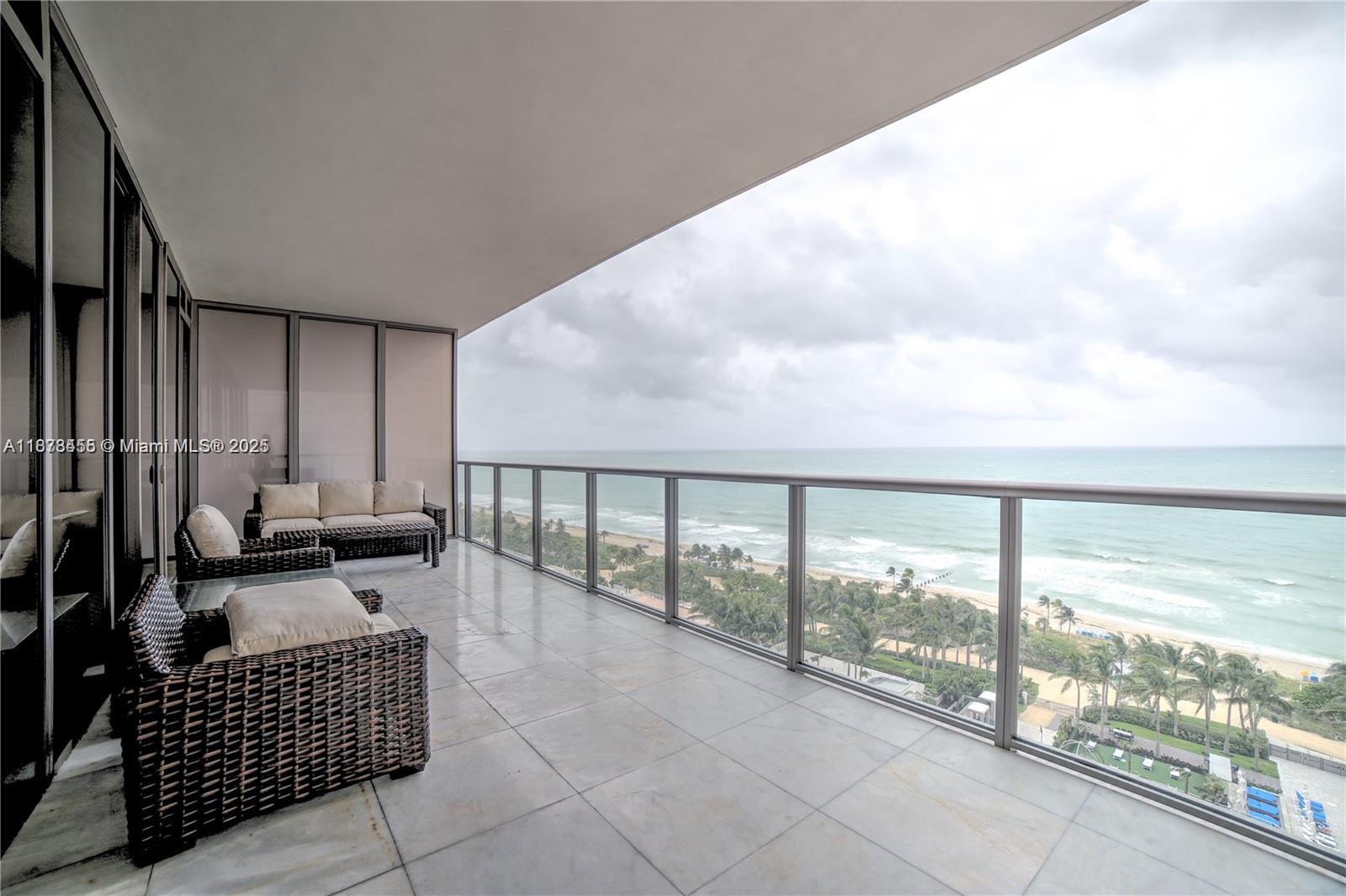 A balcony with wicker furniture overlooks a sandy beach and the ocean — 9705 Collins Ave # 1204N, Bal Harbour FL 33154, BAL HARBOUR, FL