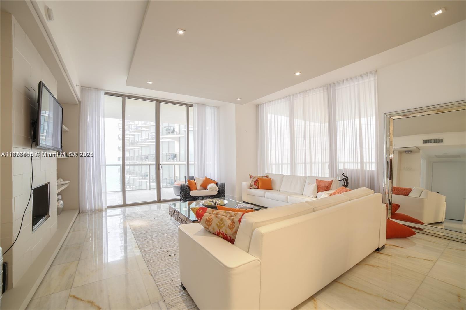 A bright living room features white sofas, marble floors, and floor-to-ceiling windows with balcony access — 9705 Collins Ave # 1204N, Bal Harbour FL 33154, BAL HARBOUR, FL