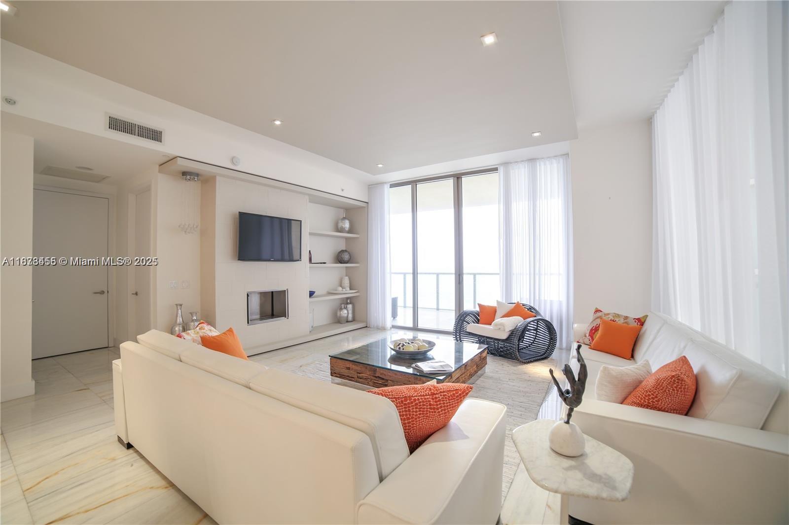 A bright living room features white leather sofas, a glass coffee table, and a fireplace — 9705 Collins Ave # 1204N, Bal Harbour FL 33154, BAL HARBOUR, FL