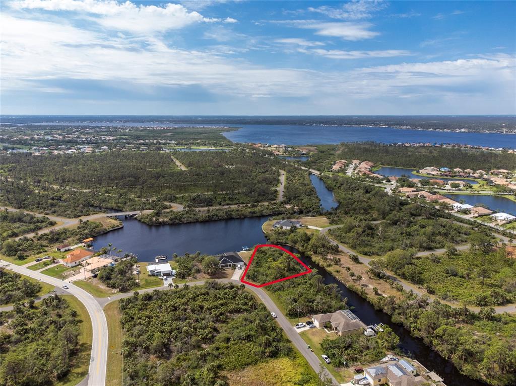 An aerial view shows a vacant, red-outlined waterfront lot surrounded by trees and residential homes — 2253 BEURKET STREET, PORT CHARLOTTE, FL