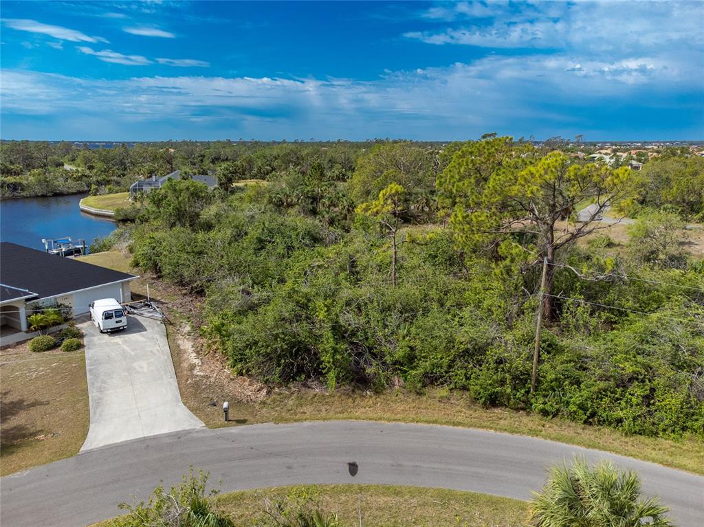 An aerial view shows a vacant, wooded lot next to a house with a driveway — 2253 BEURKET STREET, PORT CHARLOTTE, FL