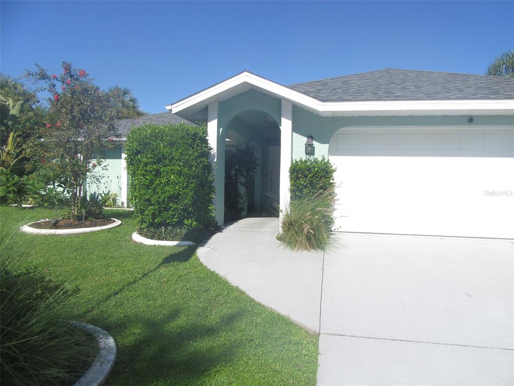 The exterior of a light green house features a garage, a covered entryway, and landscaping — 4059 MICHEL TREE STREET, PORT CHARLOTTE, FL