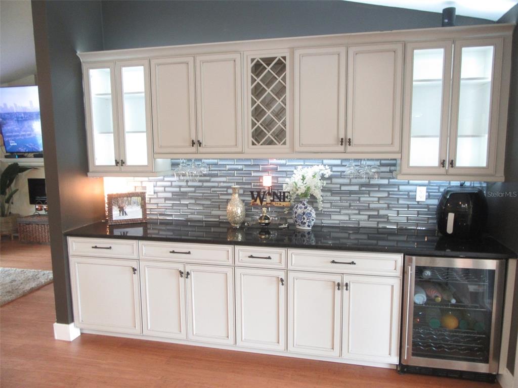 A kitchen wet bar features cream cabinets, a black countertop, and a glass tile backsplash — 4059 MICHEL TREE STREET, PORT CHARLOTTE, FL