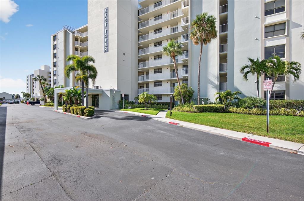 An exterior view shows the East Tower building with palm trees and a paved driveway — 300 WOODETTE DRIVE UNIT 404B, DUNEDIN, FL