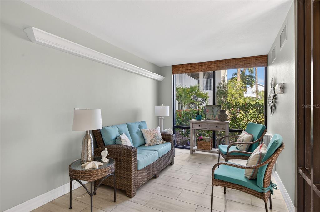 A sunroom features wicker furniture with teal cushions, tile flooring, and large windows with greenery — 300 WOODETTE DRIVE UNIT 404B, DUNEDIN, FL