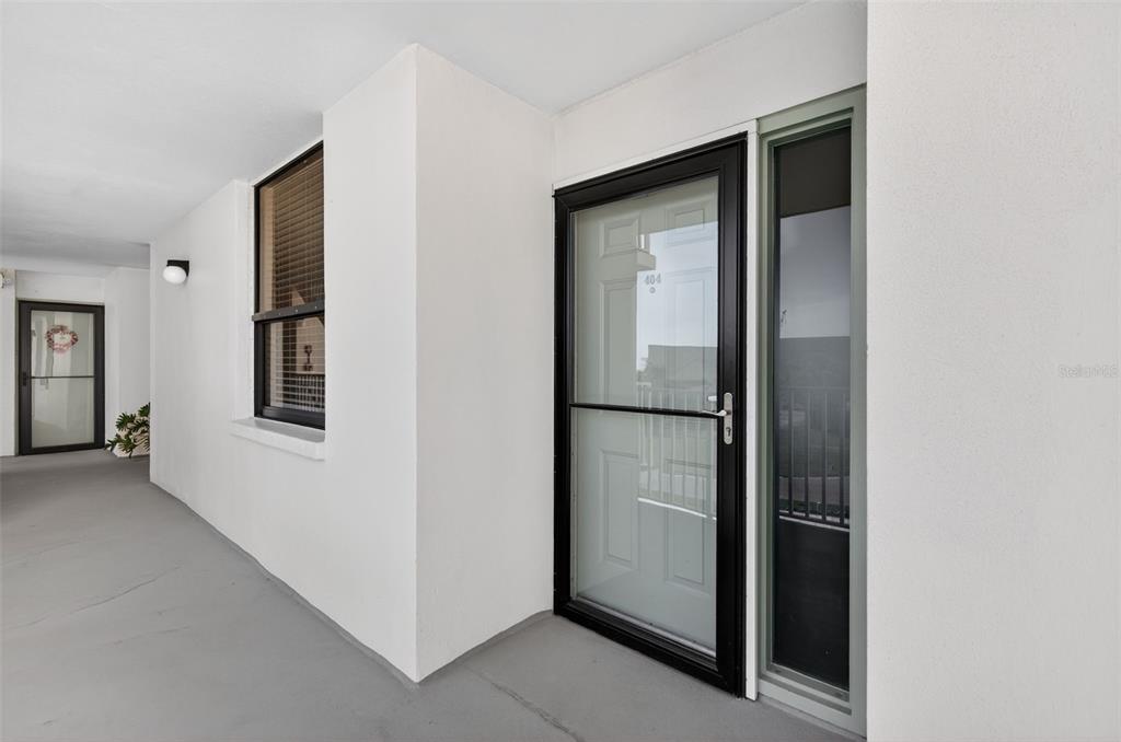 A white exterior hallway features a door labeled 404 with a black storm door — 300 WOODETTE DRIVE UNIT 404B, DUNEDIN, FL