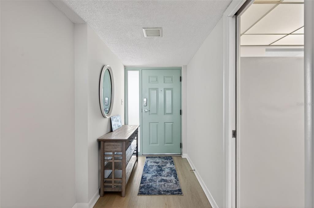 An entryway features a light blue front door, a wooden console table, and a rug — 300 WOODETTE DRIVE UNIT 404B, DUNEDIN, FL