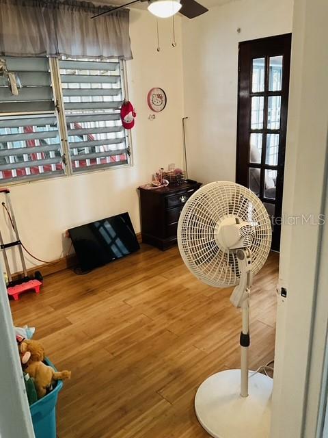 A room with wood-look flooring, a pedestal fan, a television, and a window with blinds — C-10 CLL BLANCA, BAYAMON, PR