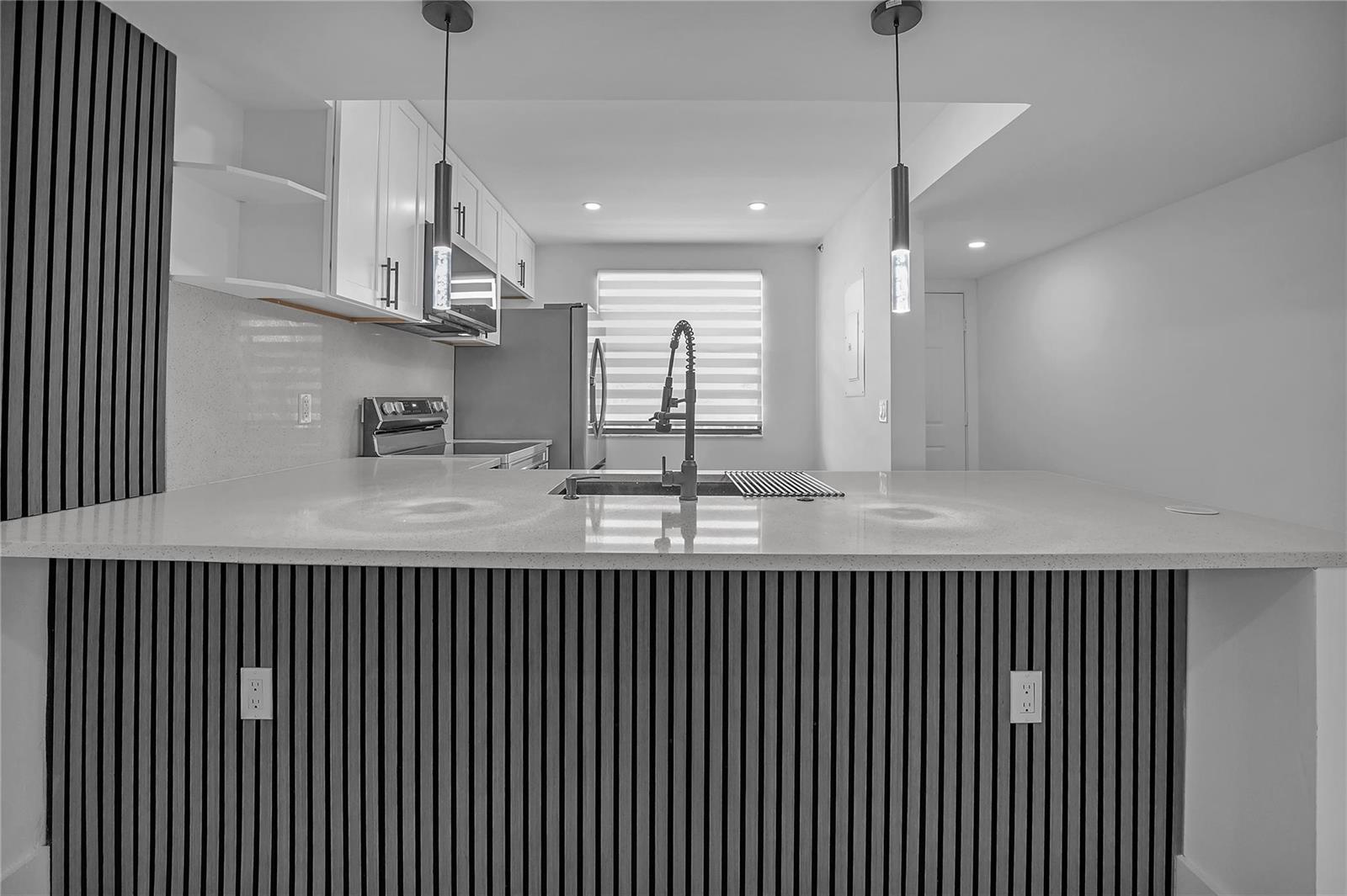 A kitchen features a white quartz island with a sink and vertical wood slat paneling — 6037 Balboa Circle # 401, Boca Raton FL 33433, BOCA RATON, FL