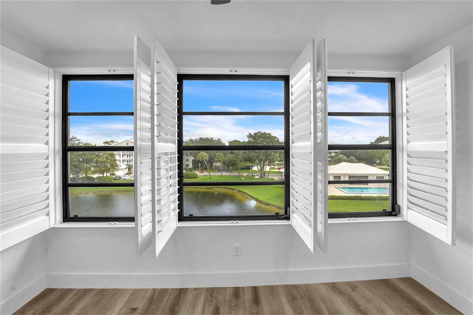 A room with light wood flooring and three windows featuring white plantation shutters overlooking a pond — 6037 Balboa Circle # 401, Boca Raton FL 33433, BOCA RATON, FL