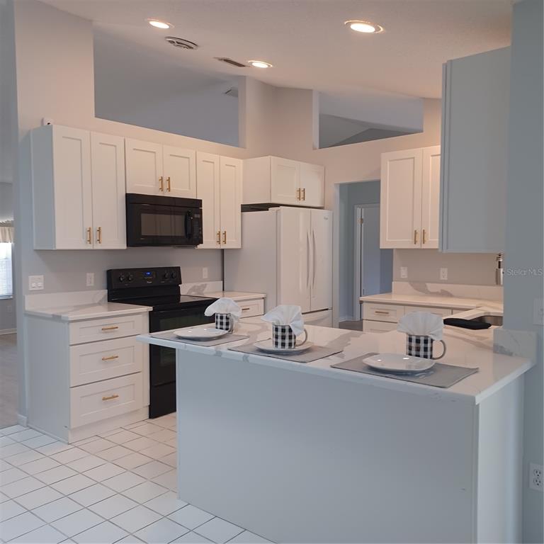 A kitchen features white cabinets, a black microwave and stove, and a white countertop island — 18 WESTCLIFFE LANE, PALM COAST, FL
